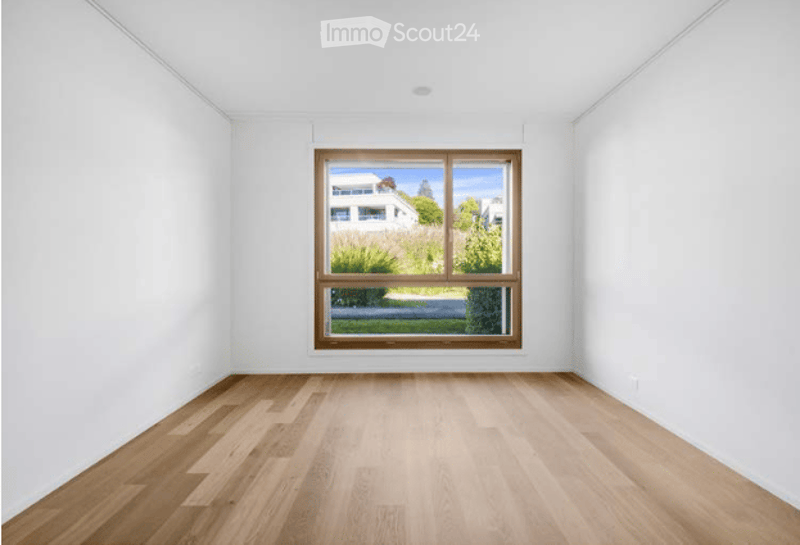 Empty room with white walls, wooden floor, and large window showing outdoor view.