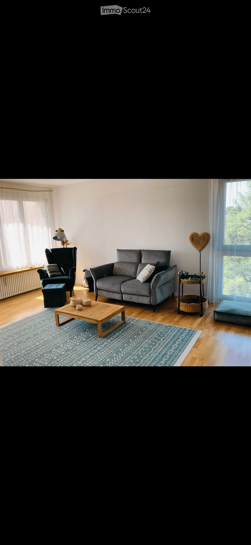 Living room with a couch, coffee table, chair, lamp, rug, and a window with a view of trees