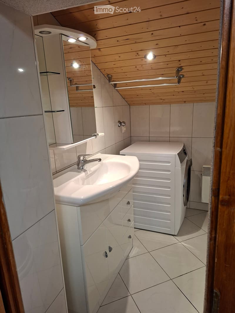 Modern bathroom with wooden ceiling, white tiled walls, a sink with a mirror, a cabinet, and a washing machine.