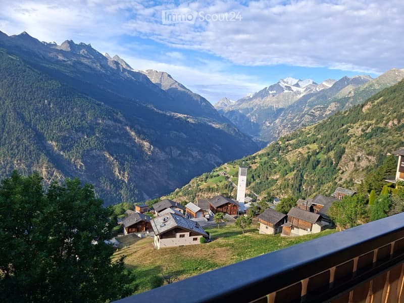 A panoramic view of a mountain valley with a small village nestled among the slopes, surrounded by dense forests and towering peaks.