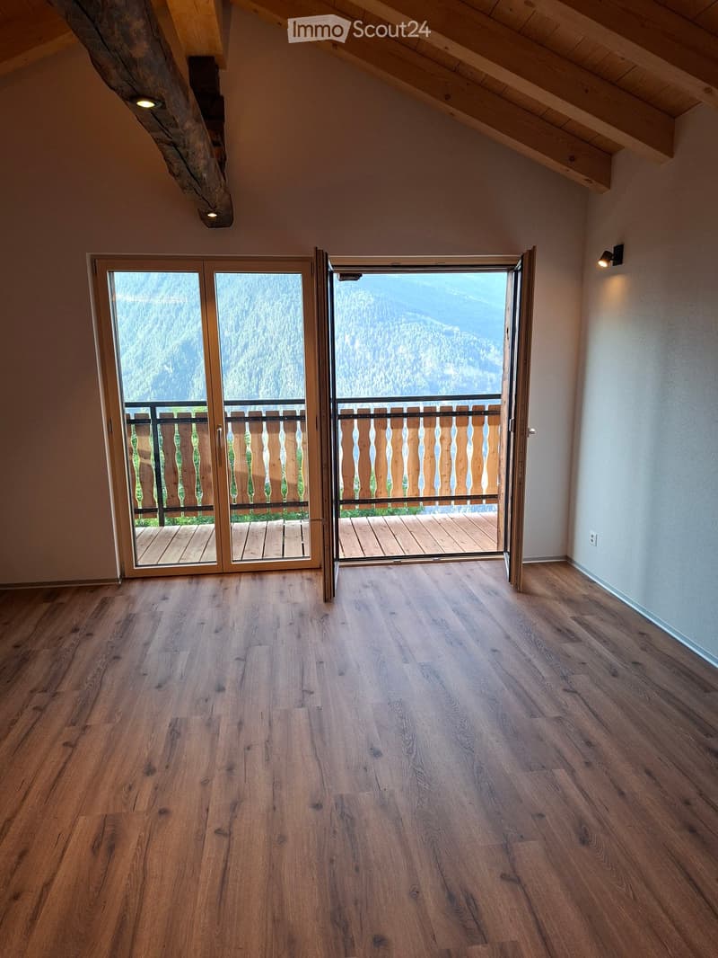 Empty room with wooden flooring, large sliding glass doors leading to a balcony with wooden decking and a scenic mountain view.
