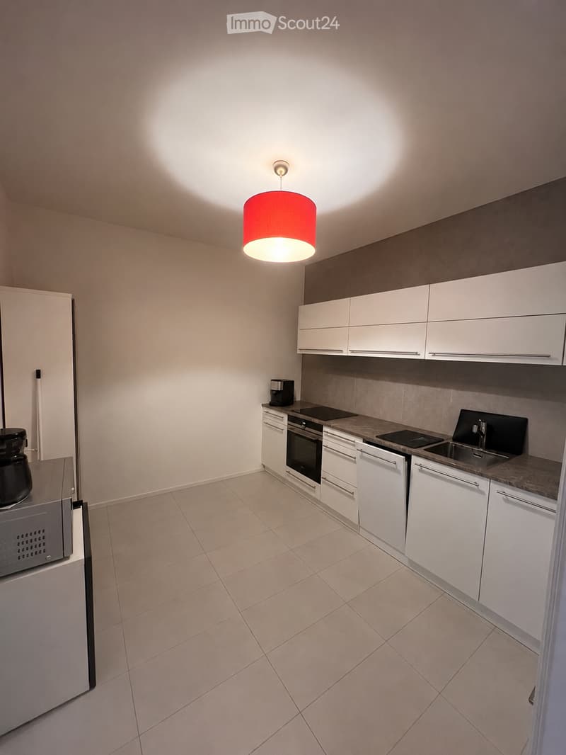 Modern kitchen with white cabinets, stainless steel appliances, and a pendant light fixture. Features a microwave, coffee maker, oven, and sink.