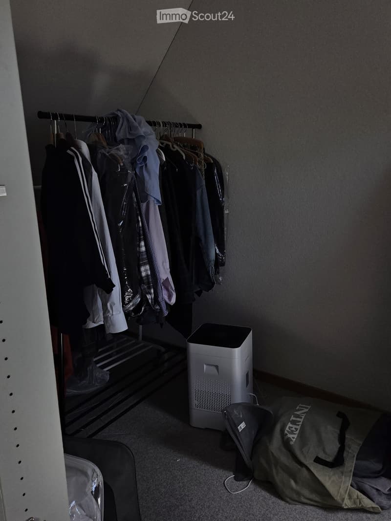 A small, furnished closet space with a wardrobe, air purifier, and a backpack on the floor.