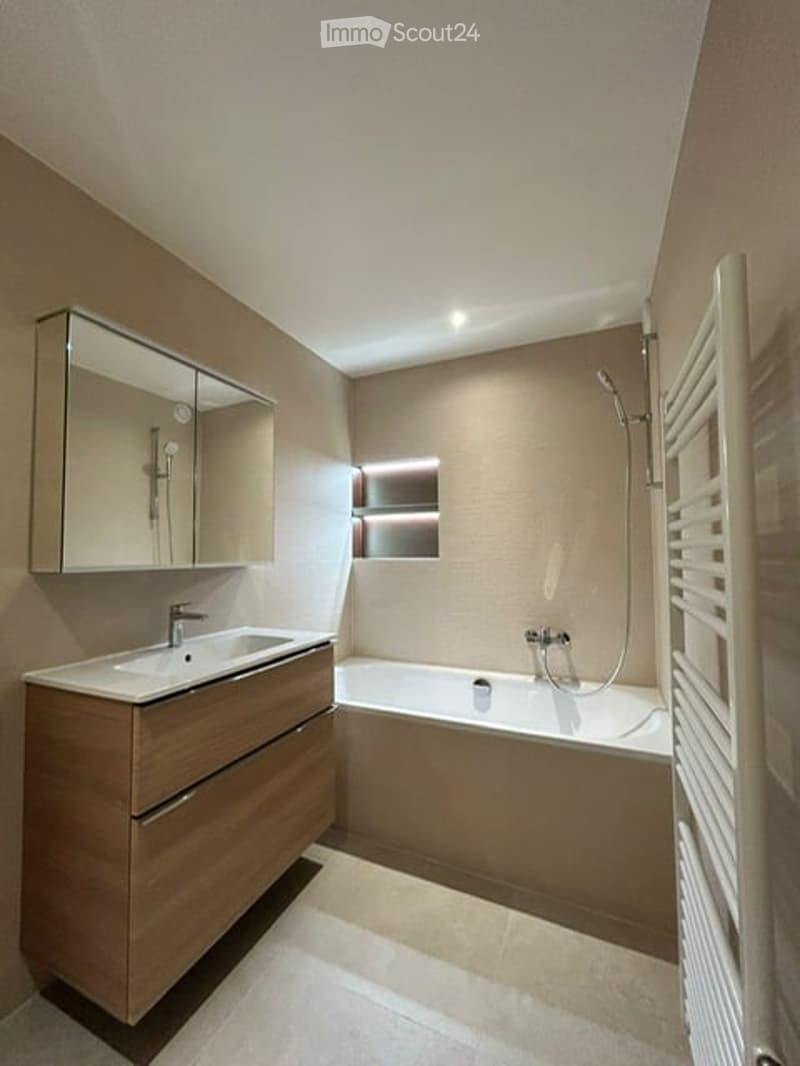Modern bathroom with a wooden vanity, sink, mirror, bathtub, and showerhead. The space features warm lighting and a clean, contemporary design.