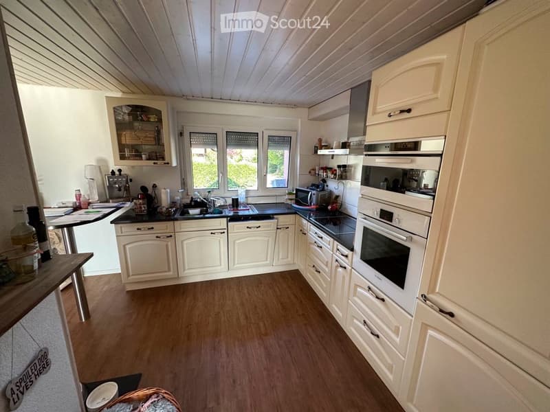 Bright kitchen with white cabinets, black countertops, and wooden flooring. Features include a sink, oven, microwave, and a small table with a lamp.