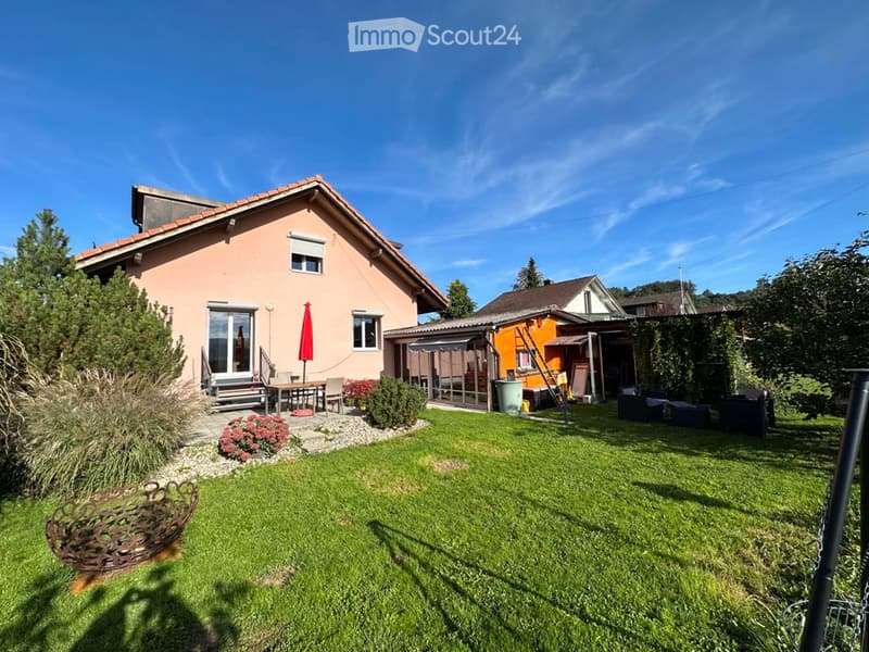 A well-maintained garden with a lawn, patio furniture, and a small seating area near the house.