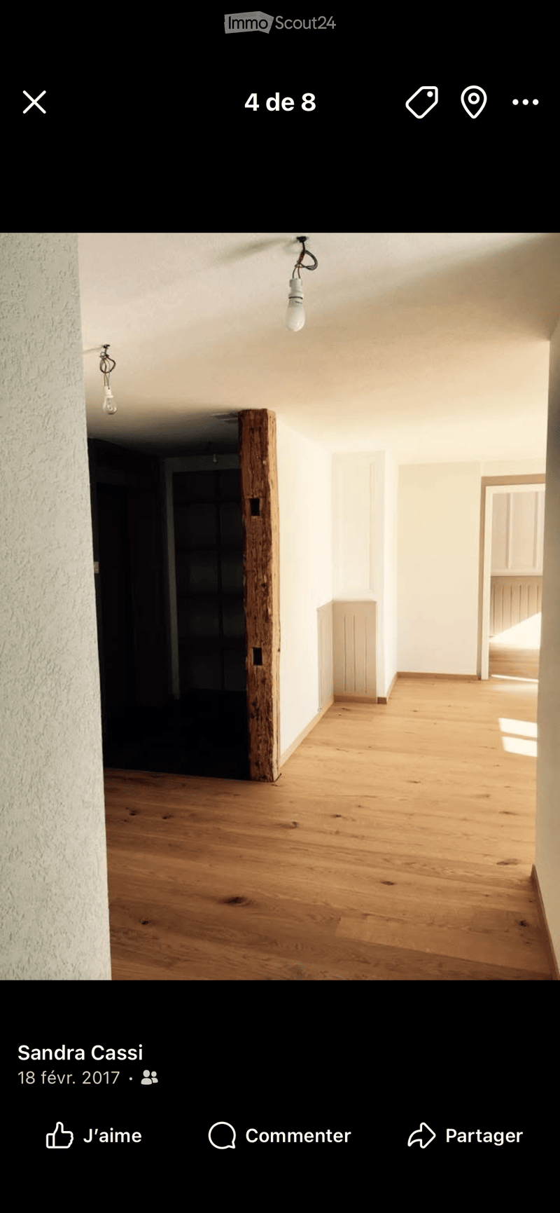 Empty room with wooden flooring, white walls, and exposed wooden beam. Two hanging light fixtures are visible.