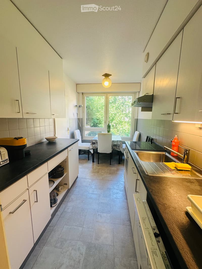 Modern kitchen with white cabinets, black countertops, and a dining area with a table and chairs. The kitchen features a sink, faucet, and various appliances.