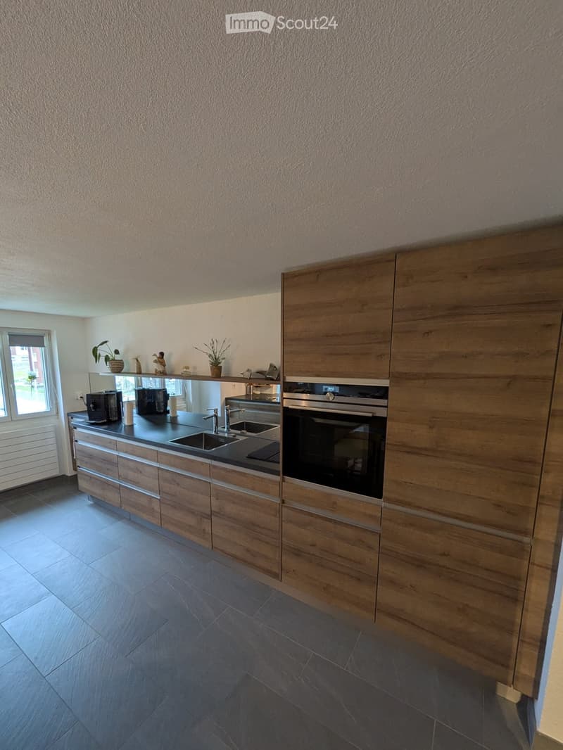 Modern kitchen with wooden cabinets, black countertop, stainless steel sink and faucet, built-in oven, and decorative items on the windowsill.