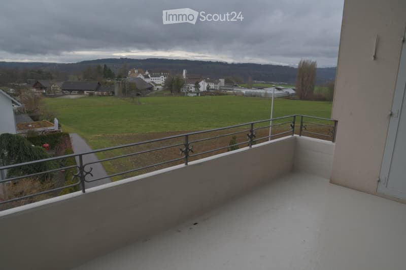 empty balcony with metal railings, overlooking a large green field and distant buildings