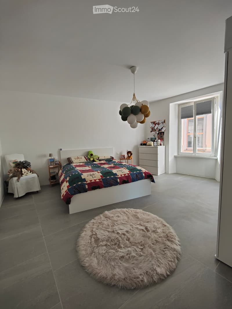 Modern bedroom with a large bed, colorful patchwork quilt, nightstand, chair, furry rug, and decorative balloons.