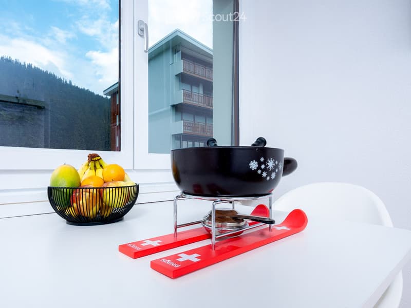 a room with a table, black bowl with fruits, cheese fondue bowl on stand