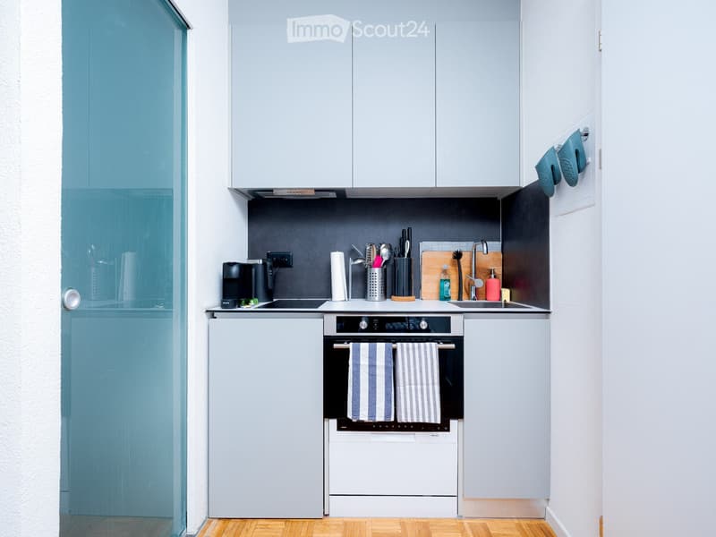compact kitchen, electric stove, built-in dishwasher, refrigerator, coffee machine, hanging towel, white cabinets, gray countertops