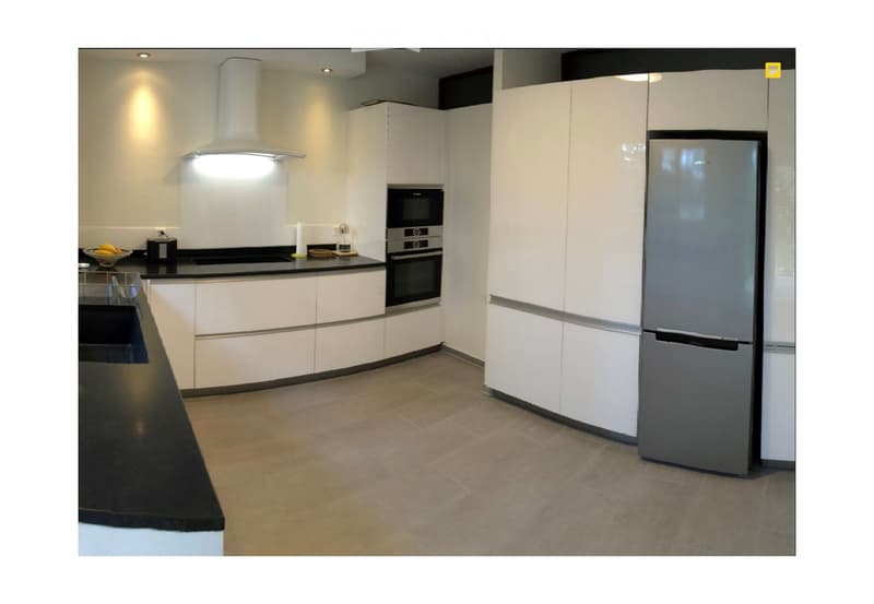 Modern kitchen with white cabinets, black countertop, stainless steel appliances including a refrigerator, oven, and microwave, and a range hood above the stove.