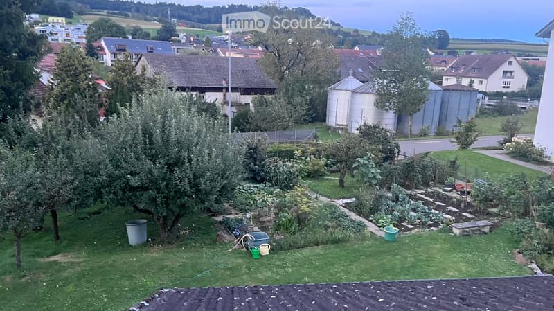 Garden with grass, fruit trees, vegetable beds, and a view of the surrounding countryside and houses.