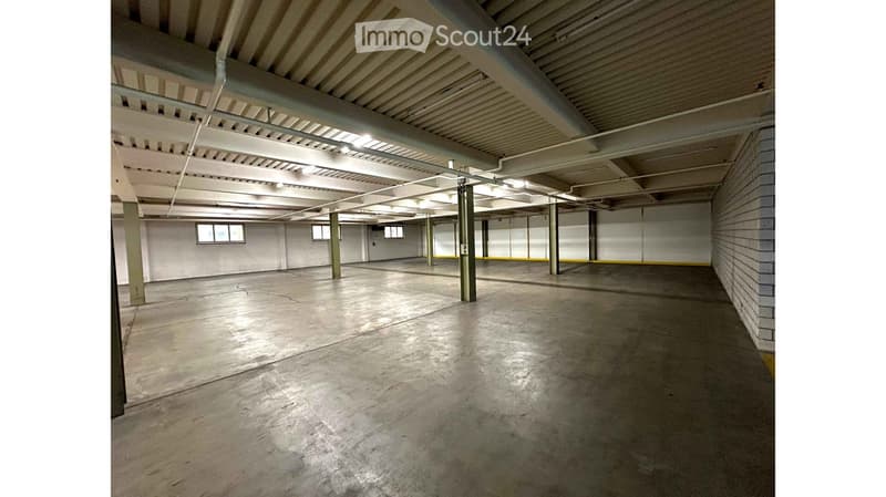 Empty garage with concrete floor, white walls, metal support columns, and small windows near the ceiling.