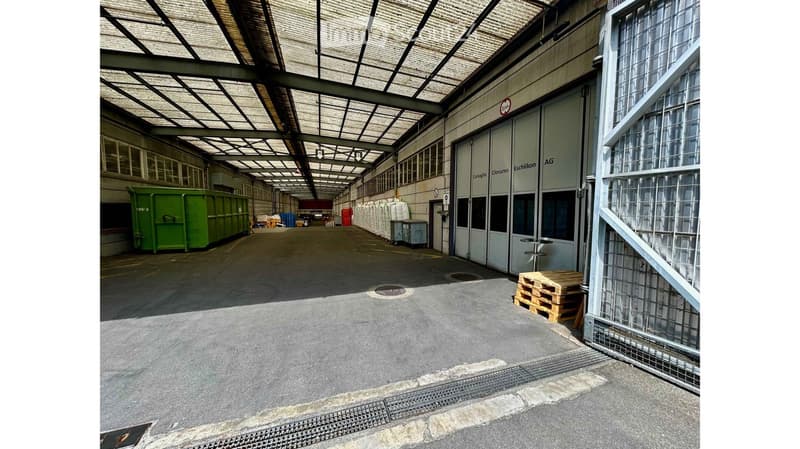 Large industrial warehouse with high ceilings, metal framework, large doors, and storage containers.