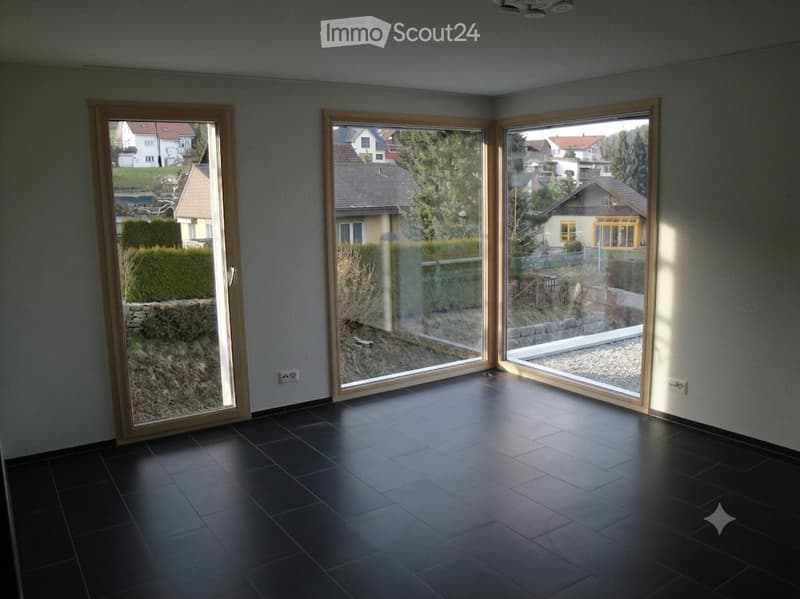 Empty room with dark tiled floor and large sliding glass doors leading to a garden area.