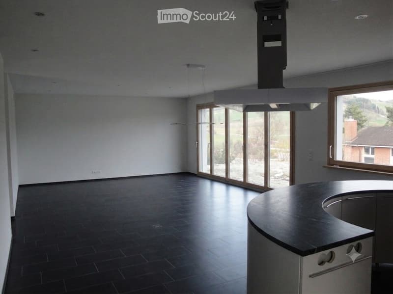 Empty room with dark tiled floor, white walls, large windows, and a kitchen island with sink.