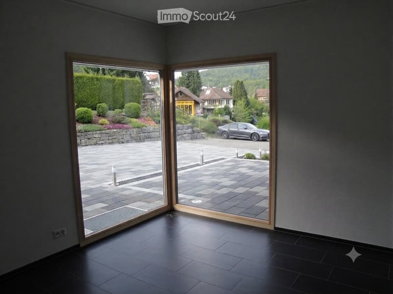 Empty room with dark tiled floor, large glass doors opening to a paved outdoor area with a car visible outside.