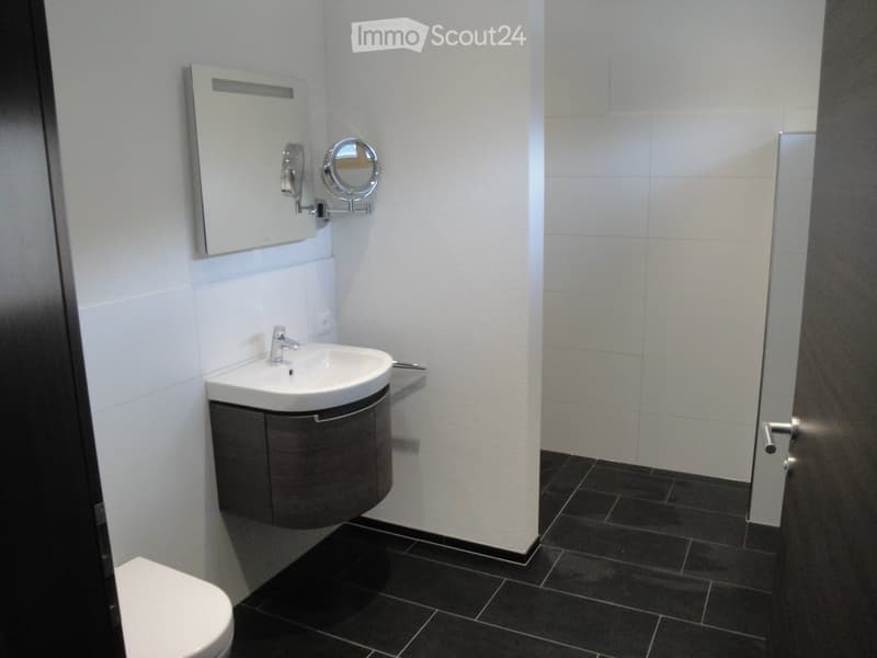 Modern bathroom with white tiled walls, black tiled floor, a white sink with a chrome faucet, a mirrored cabinet, and a toilet.