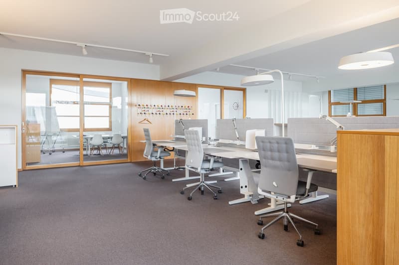 Modern office space with white desks, ergonomic chairs, large windows, and a whiteboard in the background.