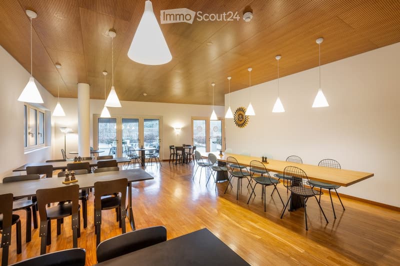 Bright, modern dining area with wooden floors, pendant lights, and multiple tables and chairs arranged for seating.