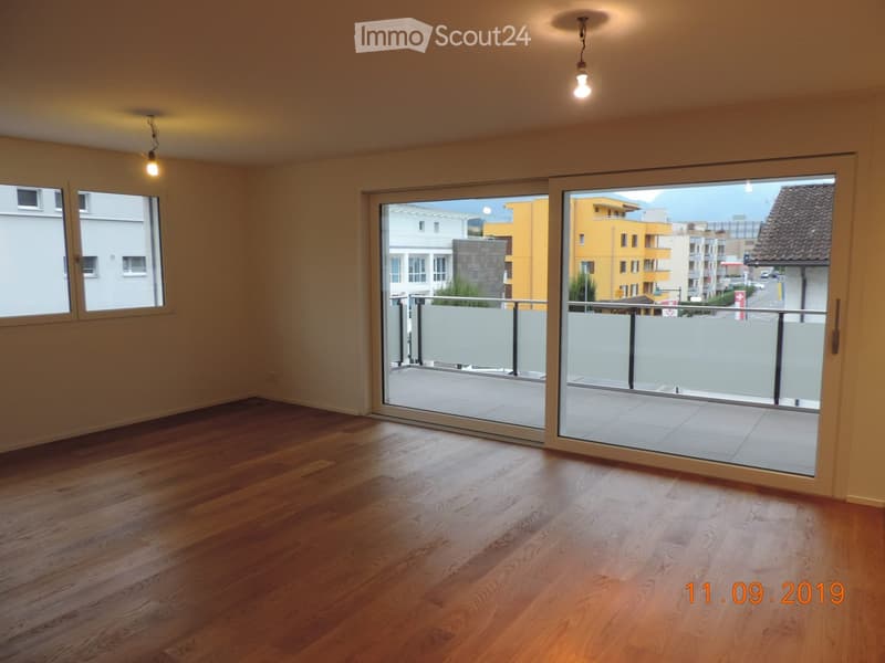 Empty room with wooden flooring, large sliding glass doors leading to a balcony, and natural light from windows.