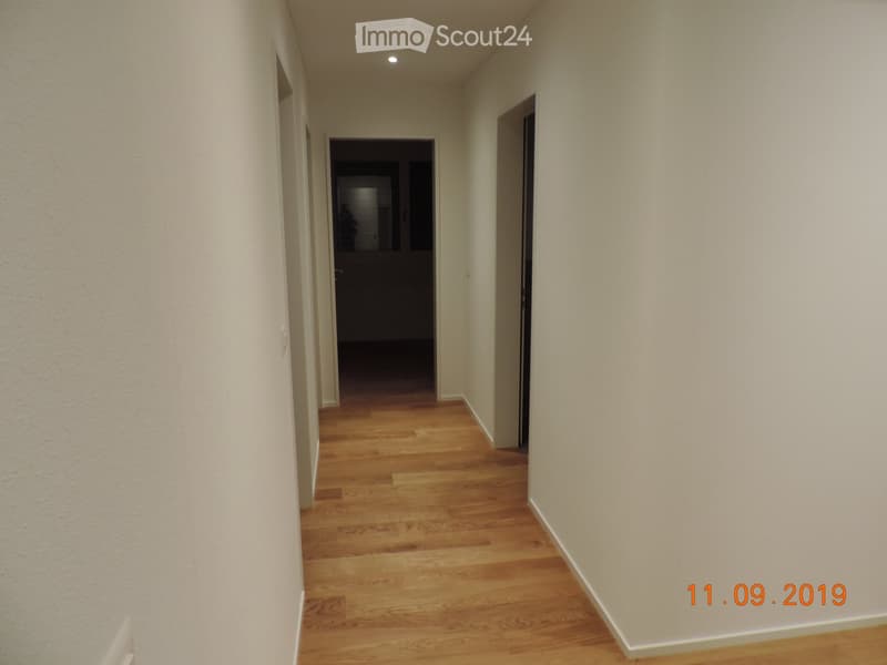 Empty hallway with wooden flooring and white walls, featuring two open doors at the end.