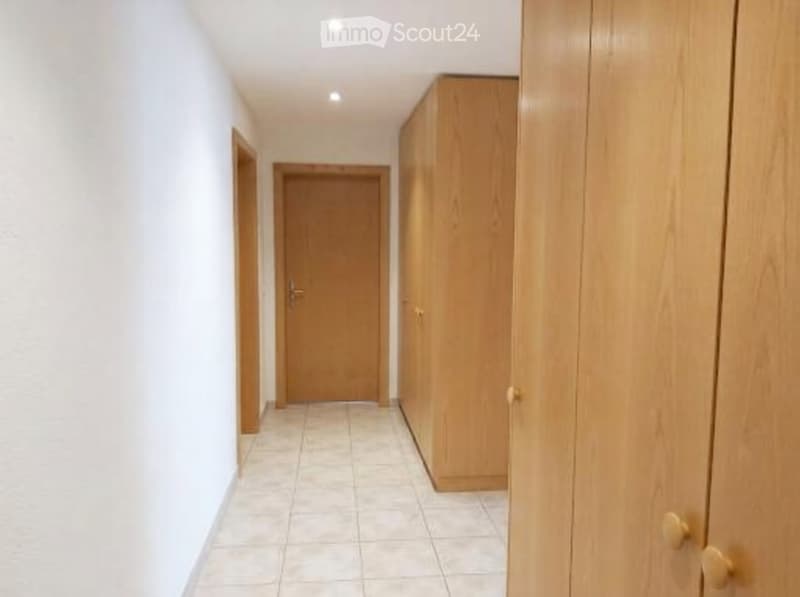 A narrow hallway with white walls, tiled floor, and wooden doors and cabinets.