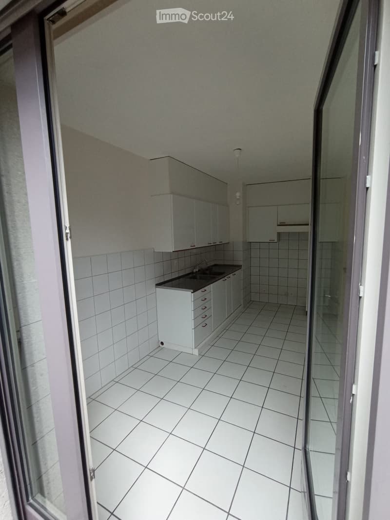 Empty kitchen with white tiled floor and walls, white cabinets, and a sink.