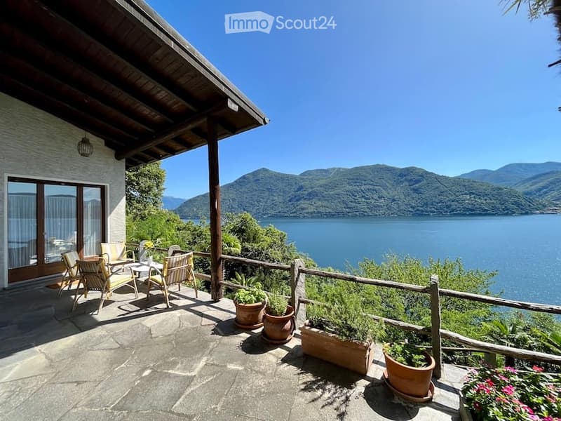 lakeside house with terrace, patio furniture, and a fence overlooking the lake and mountains
