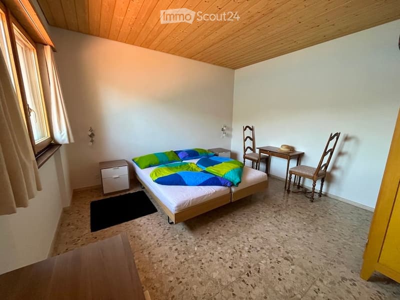 a double bed, a desk with two chairs, a cabinet with drawers, a window with curtains, wooden ceiling