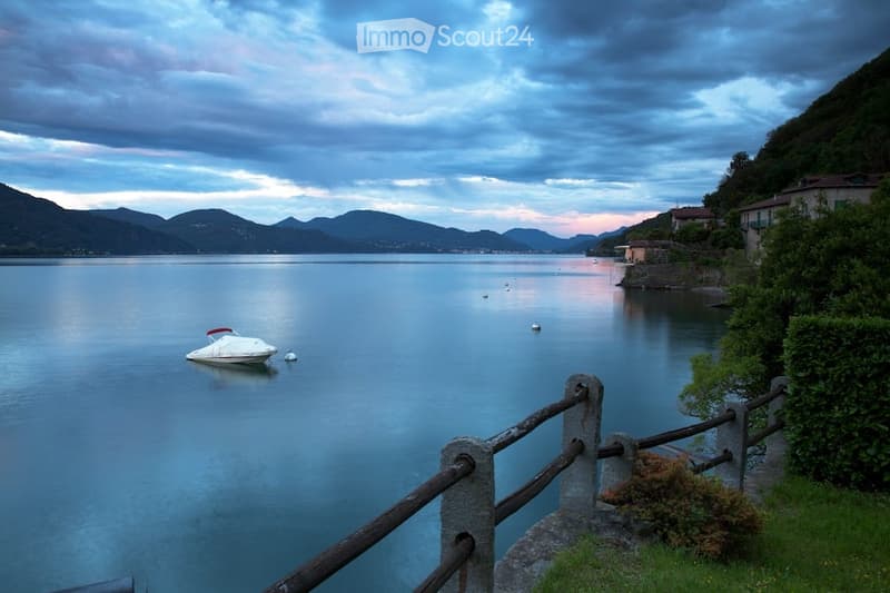 Calm lake with small boat, mountain landscape, wooden fence, greenery