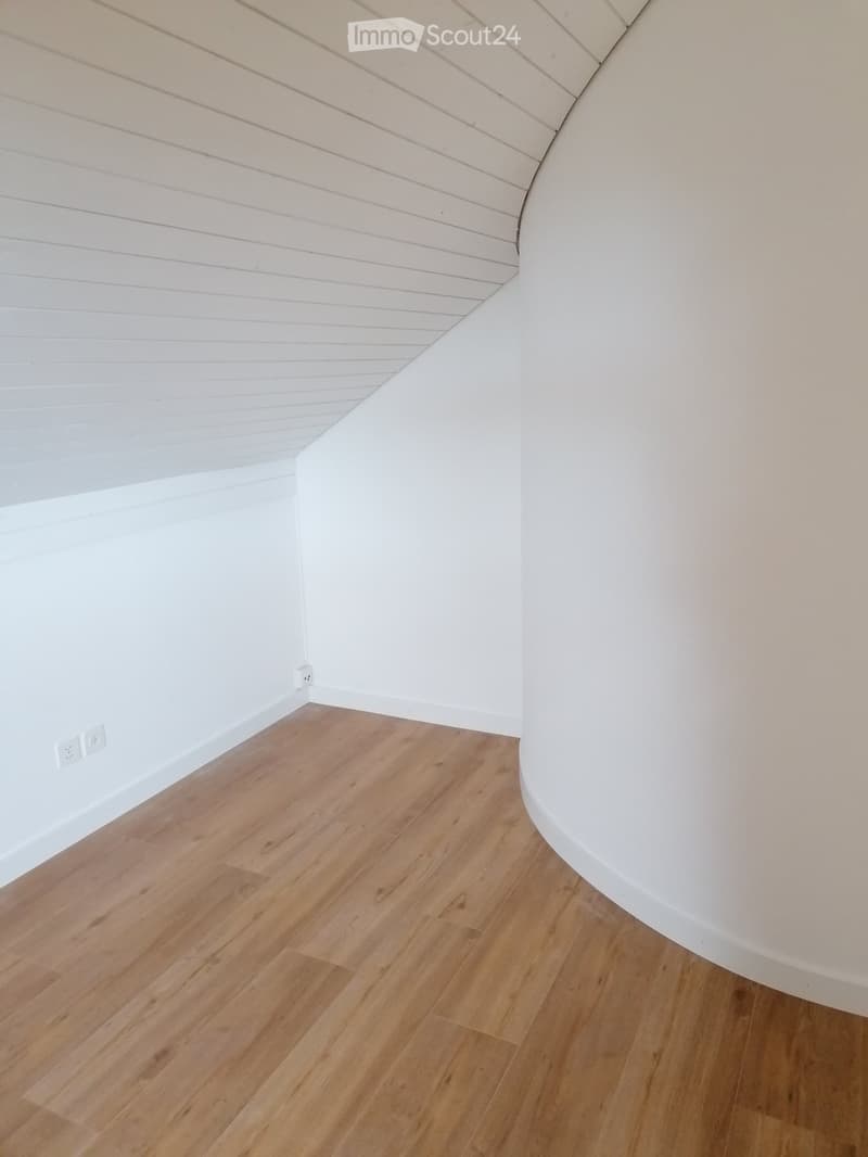 Empty room with light wooden flooring and white walls, featuring a curved white wall section and visible electrical outlets.