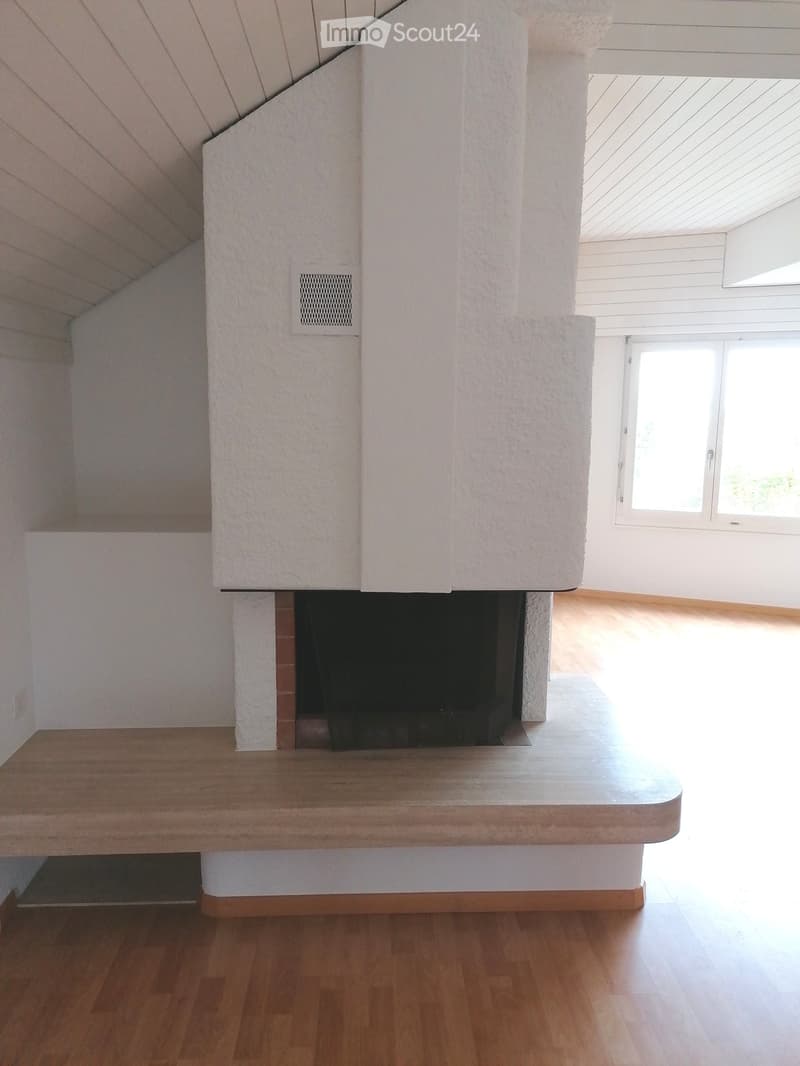 An unfurnished room with a fireplace, wooden flooring, and large windows allowing natural light to enter.