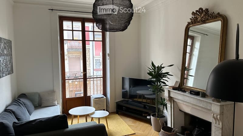 Modern living room with a grey sofa, coffee table, television, fireplace, large mirror, and a potted plant near the balcony door.