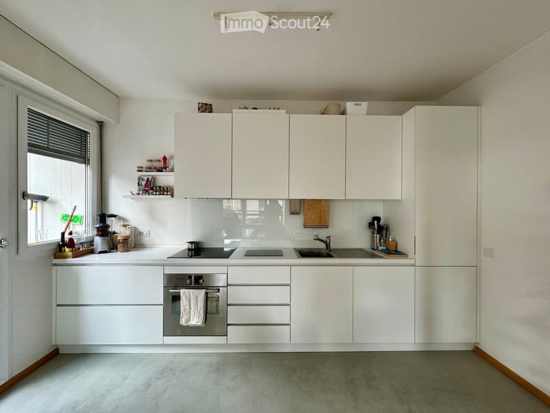 Modern kitchen with white cabinets, stainless steel appliances, and a sleek countertop. Features an oven, sink, and various kitchen items on the counter.