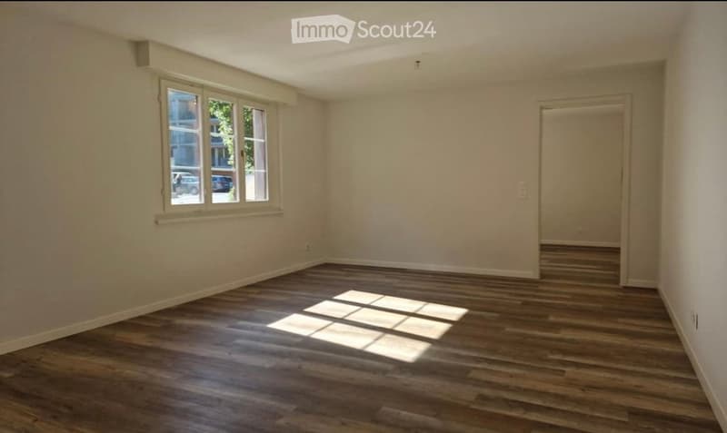 Empty room with wooden flooring, white walls, and a single window with a view of the street.