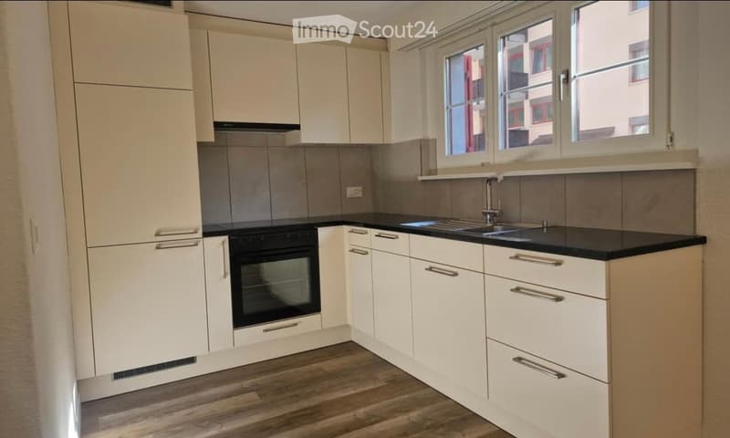 Modern kitchen with white cabinets, black countertops, and a stainless steel sink. Features include an oven and a faucet.
