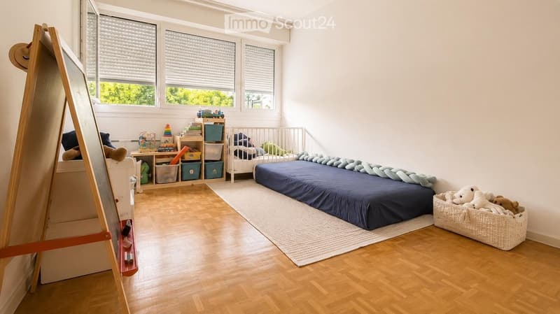 Bright, modern children's bedroom with a large bed, a crib, a toy basket, shelves with storage bins, and a wooden easel.