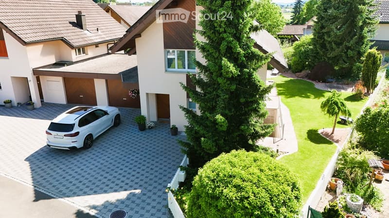 Two-story house with a garage, driveway, and well-maintained garden with trees and shrubs.