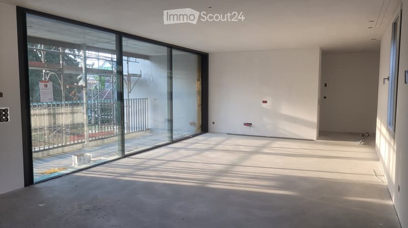 Empty room with large glass sliding doors leading to a balcony, white walls, and a concrete floor.
