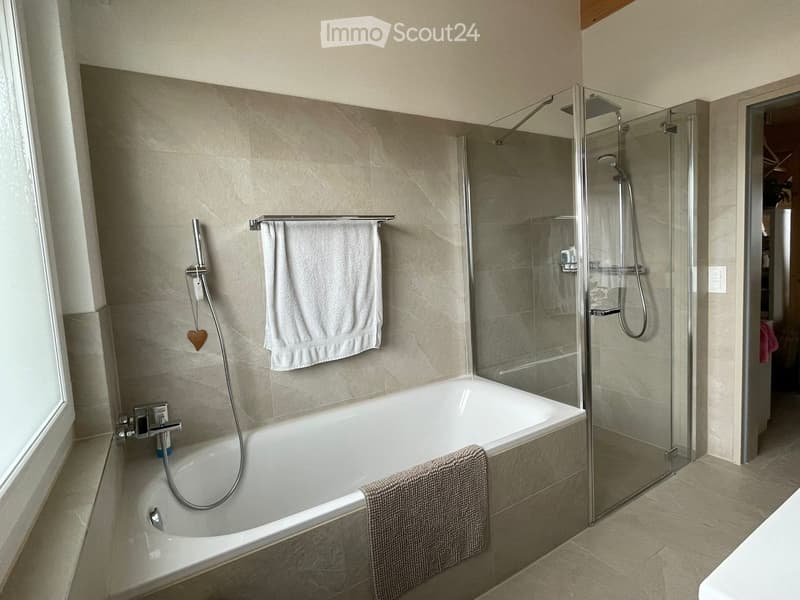 Modern bathroom with a bathtub, glass-enclosed shower, and white towels neatly placed on the walls and bathtub edge.