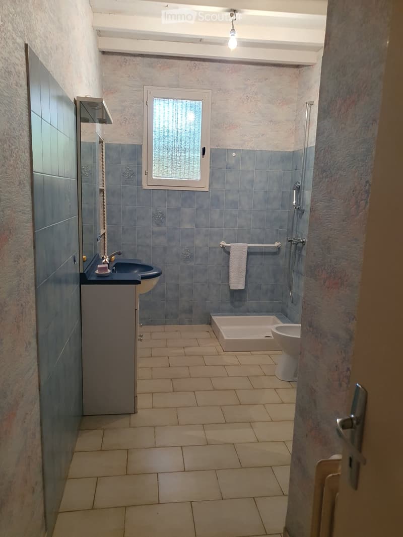 Bathroom with blue tiled walls, a sink, bathtub, toilet, and a towel on a rack.
