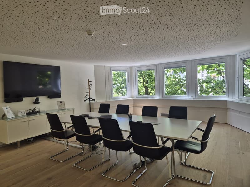 Modern conference room with a large rectangular table, black chairs, a large screen on the wall, and a cabinet with framed certificates.