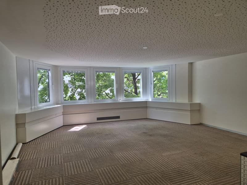 Empty room with carpeted floor, white walls, large windows, and built-in seating along one wall.