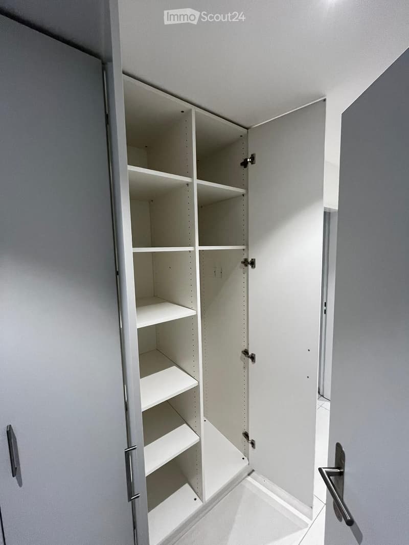Empty room with white walls, tiled floor, and open white shelving unit with multiple empty shelves.