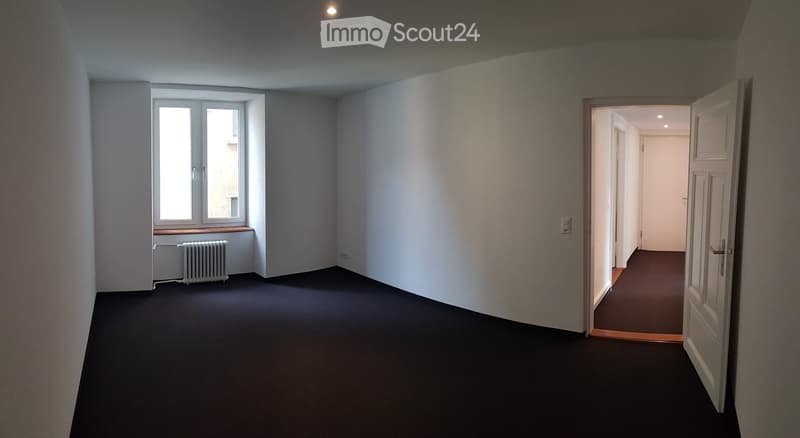 Empty room with white walls, black floor, window with white frame, radiator, open door