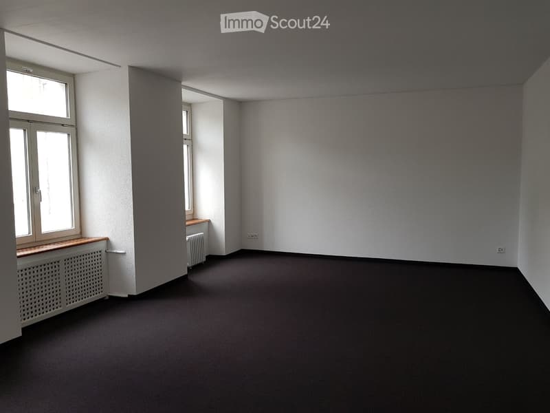 Empty room with white walls, black floor, two windows, wooden window sills, and a radiator.